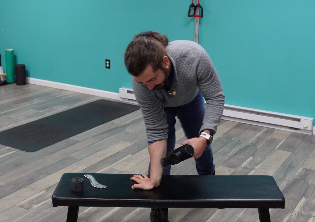 Dr. John using a massage gun in the forearm to help loosen up the muscles and connective tissue to improve wrist extension